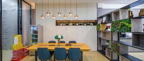 A modern dining area with a wooden table, four chairs, hanging pendant lights, and shelves with decorative items.