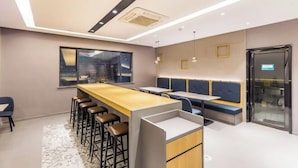 A modern kitchen with a long counter, stools, and a seating area with benches. - Ruyi Hotel (Foshan Nanhai Songgang Avenue) (Foshan)