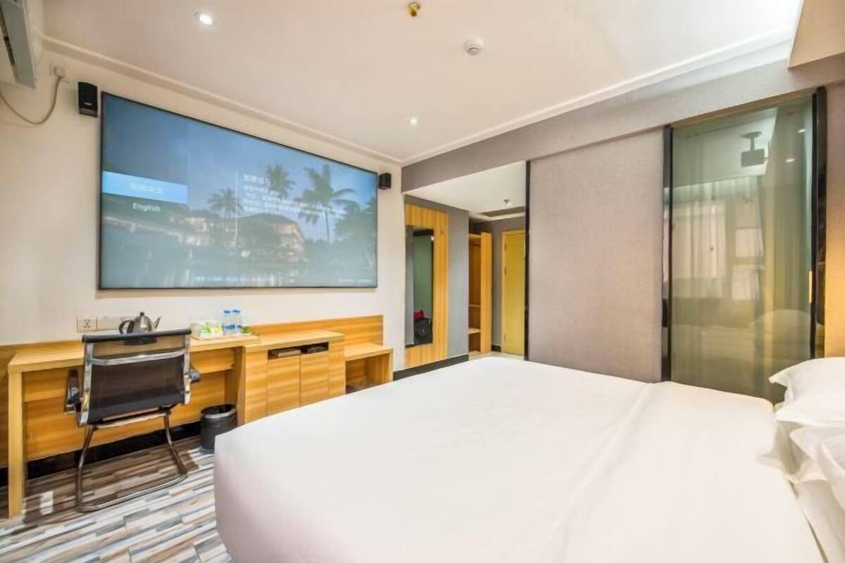 A hotel room with a large bed, a desk with a computer, a flat-screen TV, and a sliding glass door to the outside.