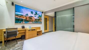 Habitación de hotel con cama, escritorio con silla, televisor montado en la pared y un ventanal grande.
