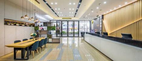 Eine moderne Hotellobby mit einer Rezeption, einem Essbereich mit langem Tisch und Stühlen sowie einer Rezeptionstheke mit vertikaler Holzpaneelgestaltung.
