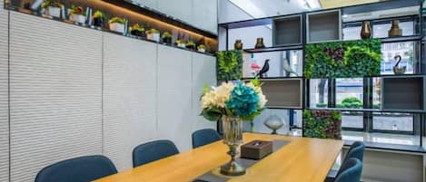 Un salón de conferencias con una larga mesa, sillas y un jarrón decorativo.