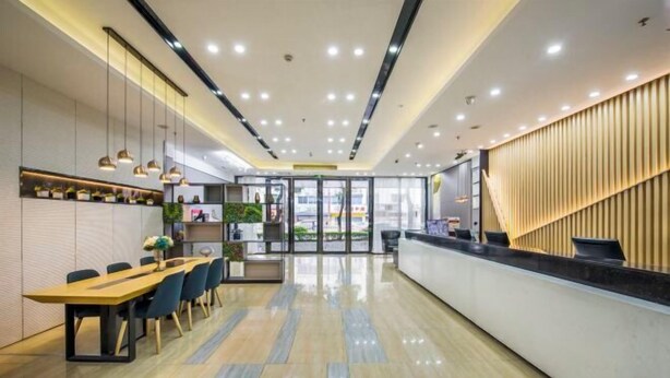 A modern hotel lobby with a reception desk, a seating area with a long table, and a staircase. - Ruyi Hotel (Foshan Nanhai Songgang Avenue) (Foshan)