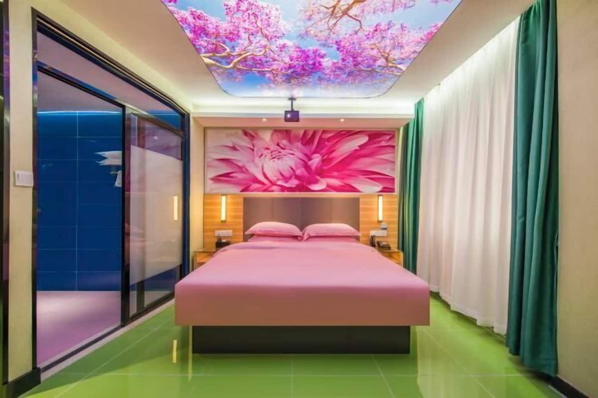 A hotel room with a large bed, a ceiling with a floral mural, and a sliding door on one side.