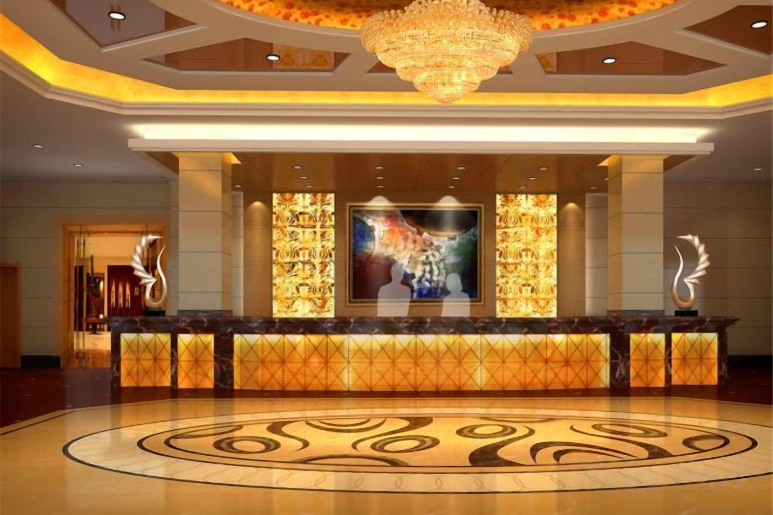 A hotel reception area with a central counter, a large chandelier, and a circular floor design.