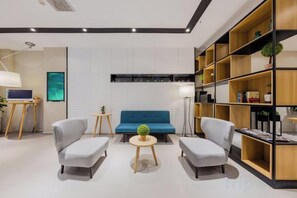 A modern living room with a blue sofa, two grey armchairs, a small round table, and a bookshelf. - Homeinn Selected Hotel (Nanjing Xiongzhou Subway Station Jinning Plaza) (Nanjing)