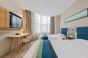 Een hotelkamer met een bureau, twee bedden, een televisie en een groot raam.