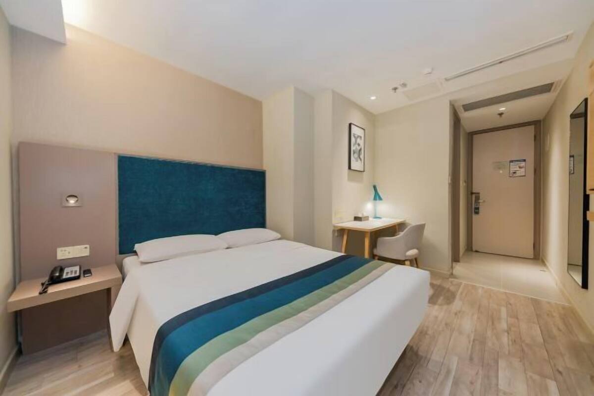 A hotel room with a bed, bedside table, lamp, and a door leading to another room.
