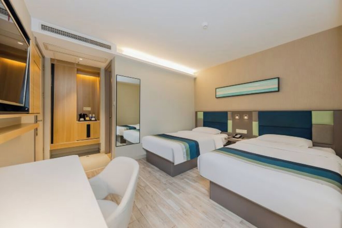 Een hotelkamer met twee bedden, een bureau, een stoel, een televisie en een spiegel.