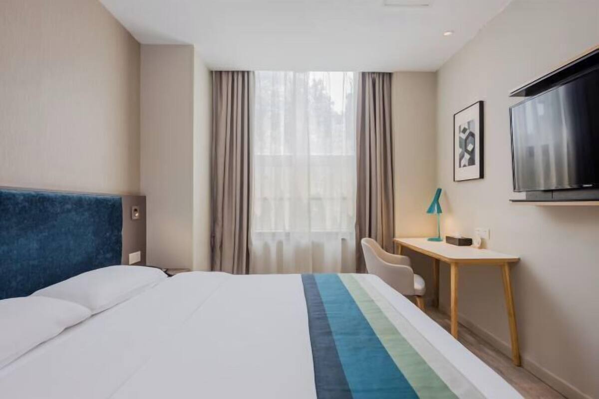 A hotel room with a bed, a desk, a chair, a TV, and a window with curtains.