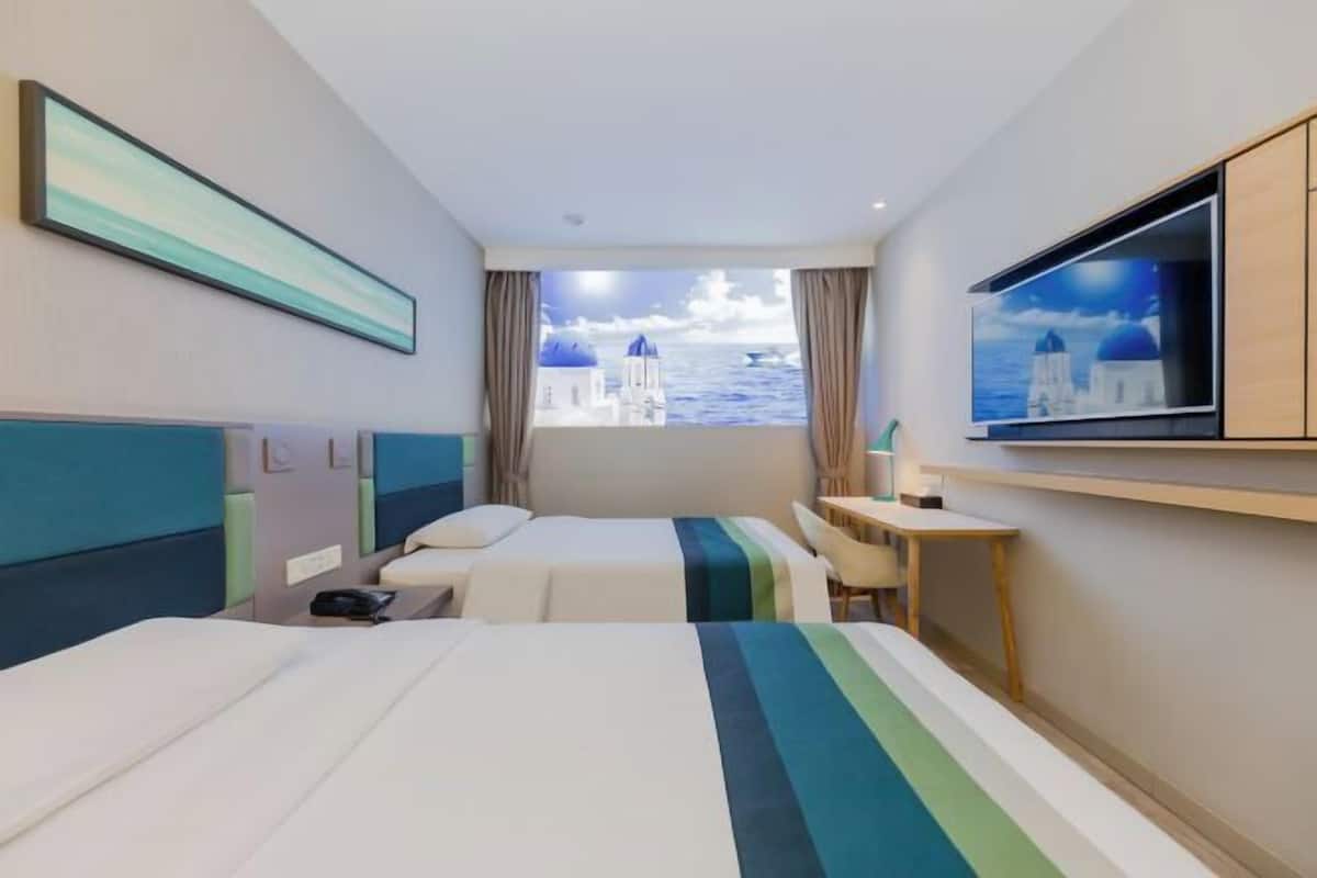 A hotel room with two beds, a desk, a TV, and a view of the sea.