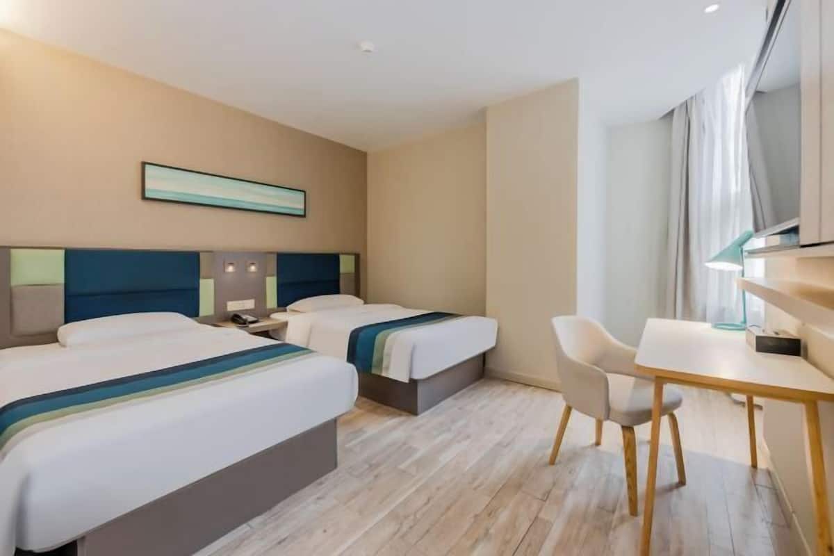 A hotel room with two beds, a desk, a chair, and a large window.