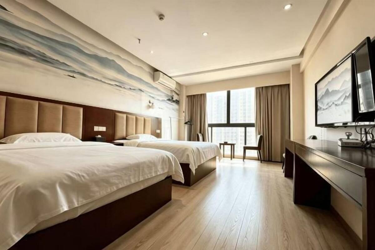 Een hotelkamer met twee bedden, een televisie, een bureau en een groot raam.