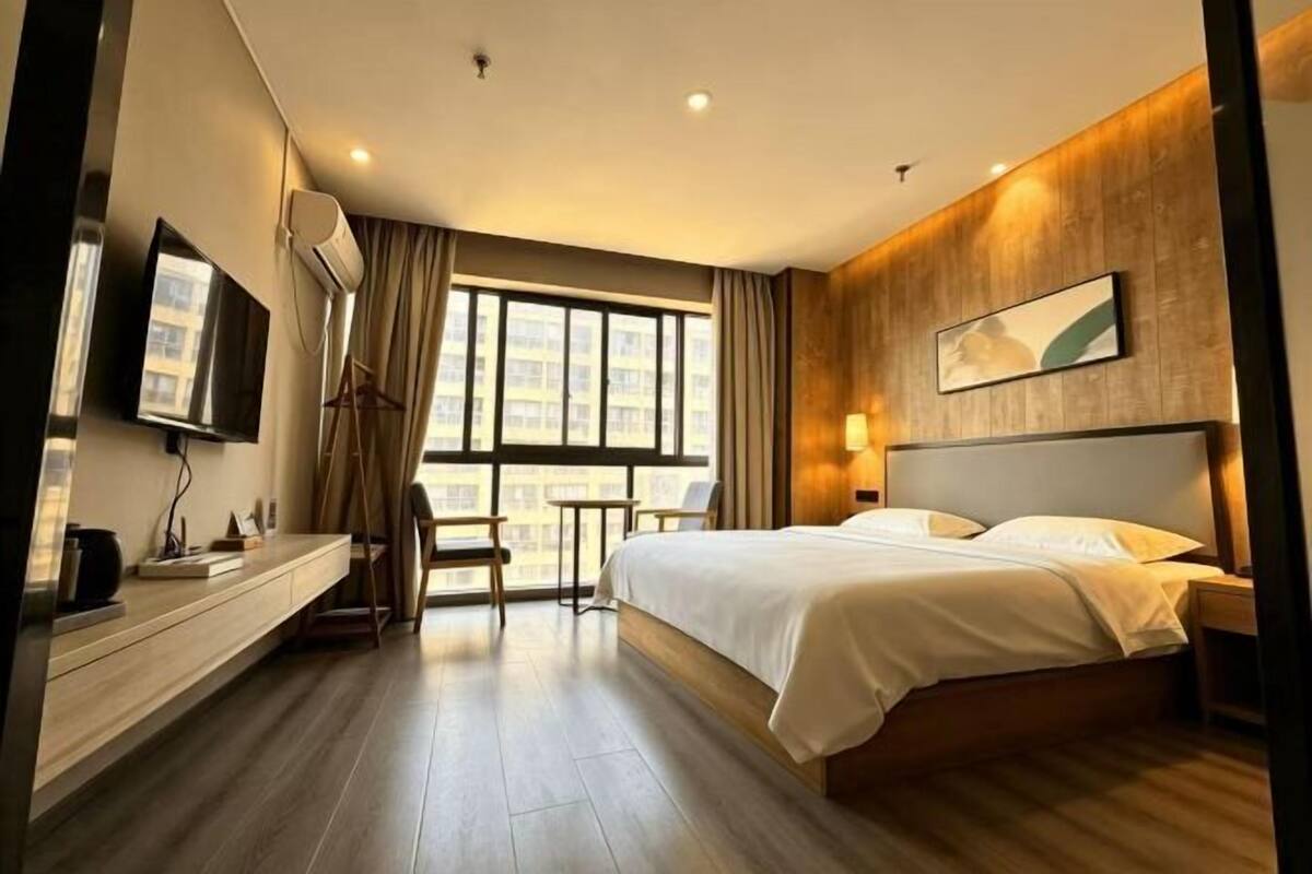 Een hotelkamer met een bed, nachtkastje, televisie en een raam met gordijnen.