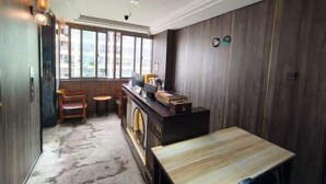 A room with a wooden desk, a small table, a radiator, and a window with a view. - Boke City Art Hotel (Wuhu)