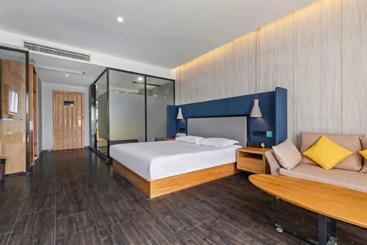 Een moderne hotelkamer met een groot bed, een bank, een kleine tafel en een glazen scheiding.