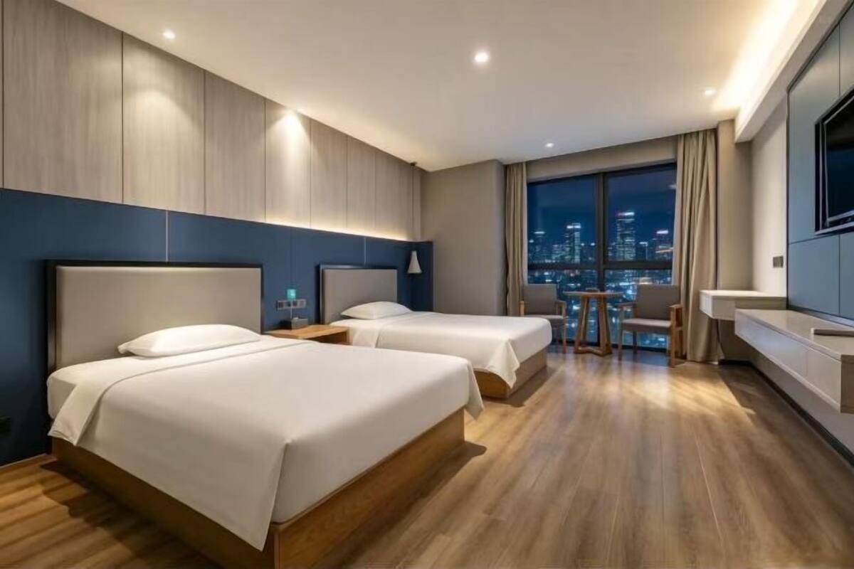 Een hotelkamer met twee bedden, een televisie, een bureau en uitzicht op de stad.