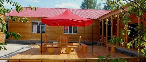 A wooden cabin with a red roof, a deck with outdoor furniture, and a covered seating area.