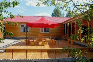 Eine Holzhütte mit rotem Dach, einer Terrasse mit Gartenmöbeln und einem überdachten Sitzbereich.