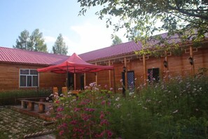 A wooden building with a red roof, a covered outdoor seating area, and a garden with pink flowers.