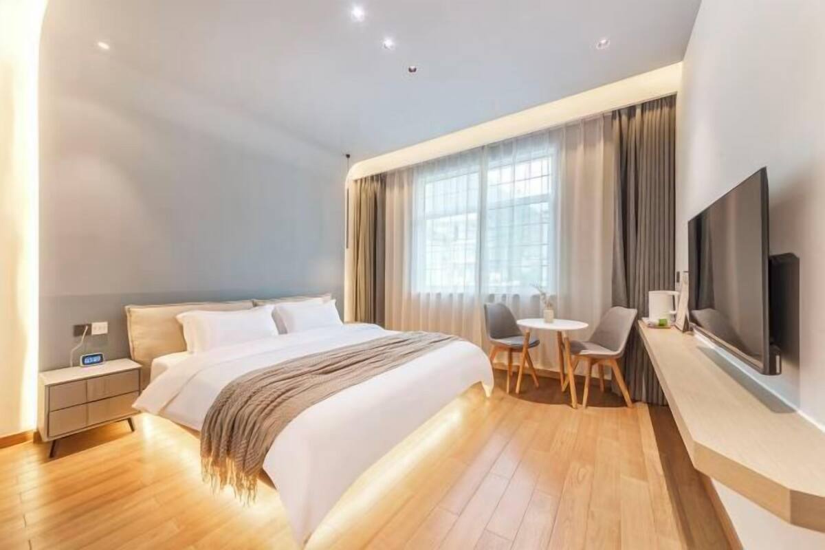 Ein modernes Hotelzimmer mit einem großen Bett, einem Schreibtisch mit Stuhl, einem Flachbildfernseher und einem Fenster mit Vorhängen.