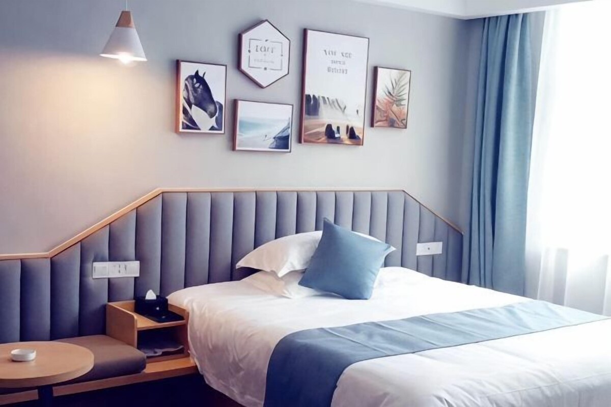 A modern hotel room with a bed, bedside table, and a wall with framed pictures.