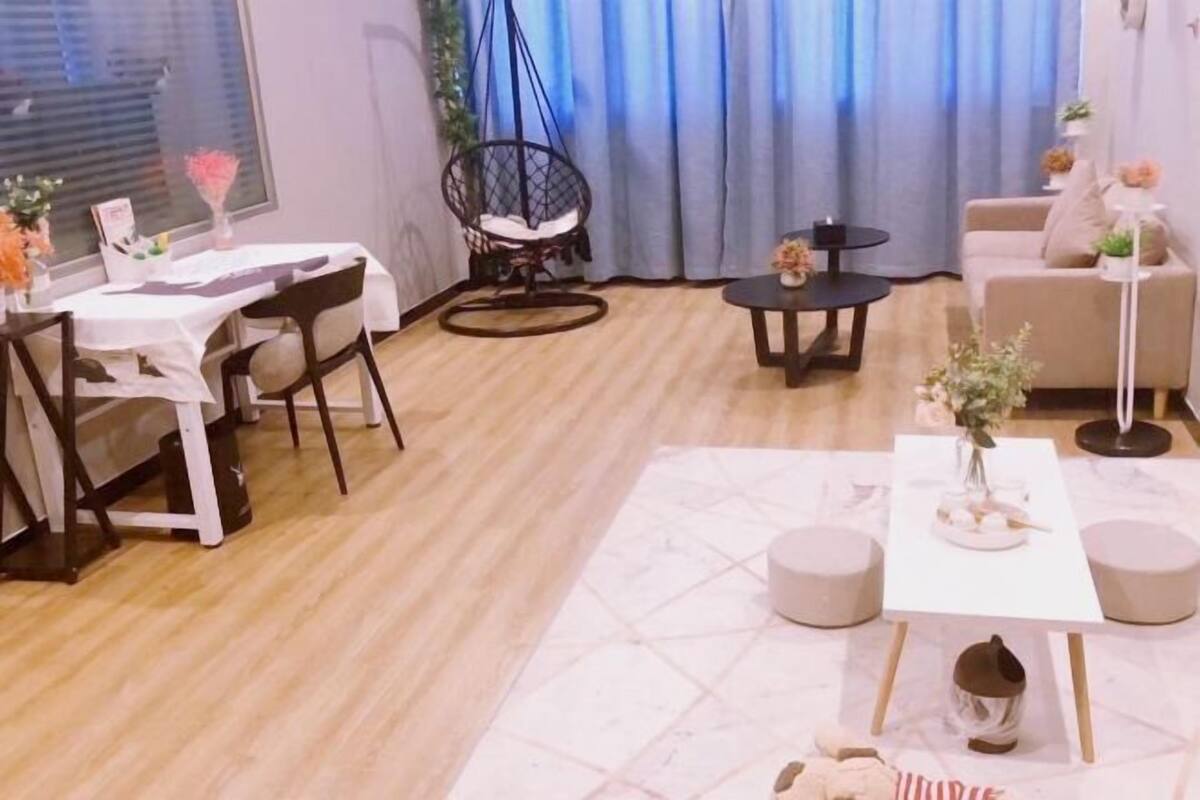A modern living room with a dining area, a hanging chair, a sofa, and a small table with a vase of flowers.