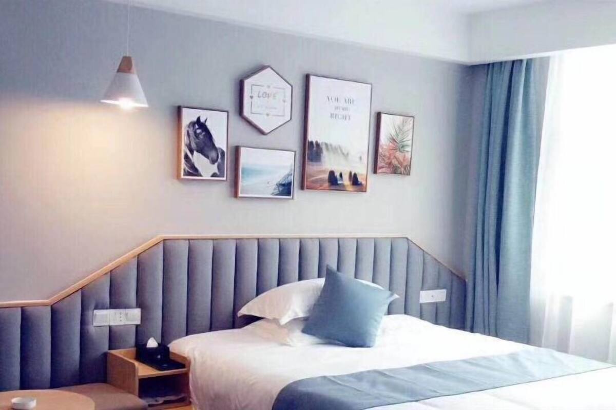 A hotel room with a bed, bedside tables, a wall-mounted lamp, and framed pictures.