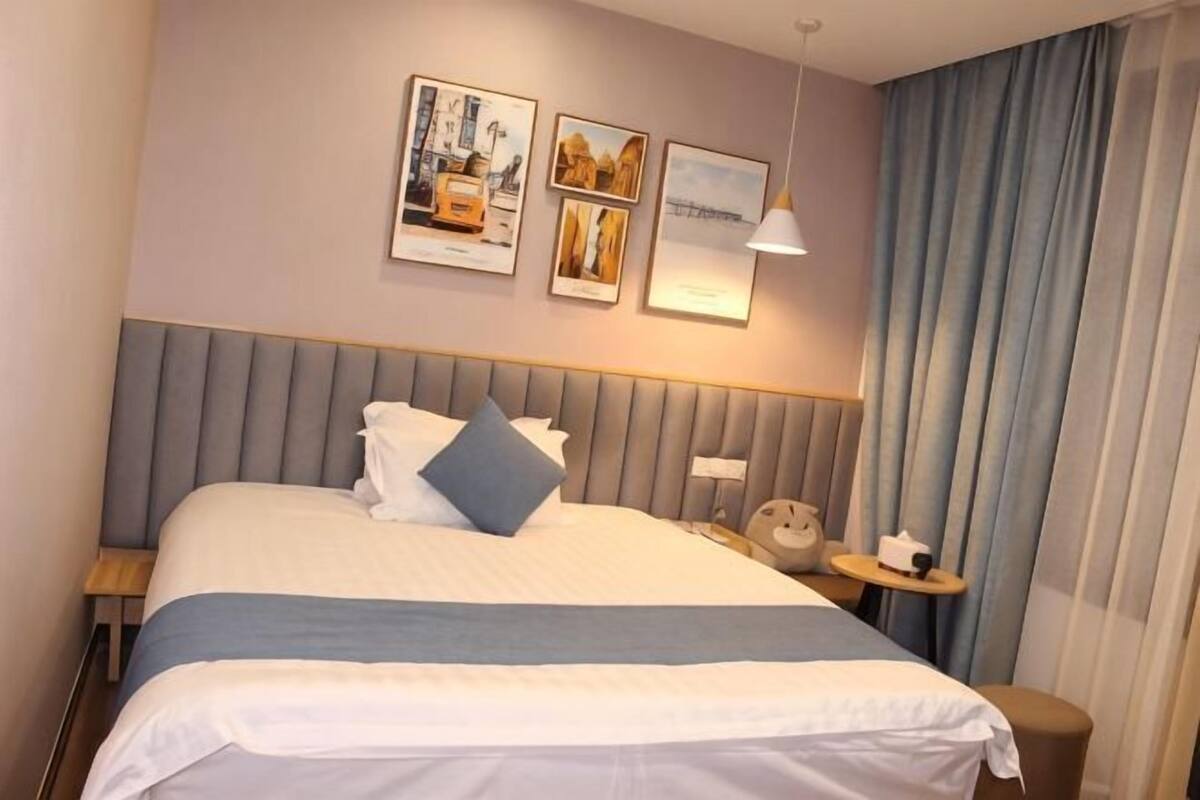 A neatly made bed with a headboard, a bedside table with a lamp, and a wall with framed pictures.