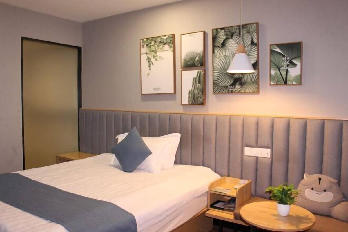 A hotel room with a bed, bedside table, lamp, and wall art.