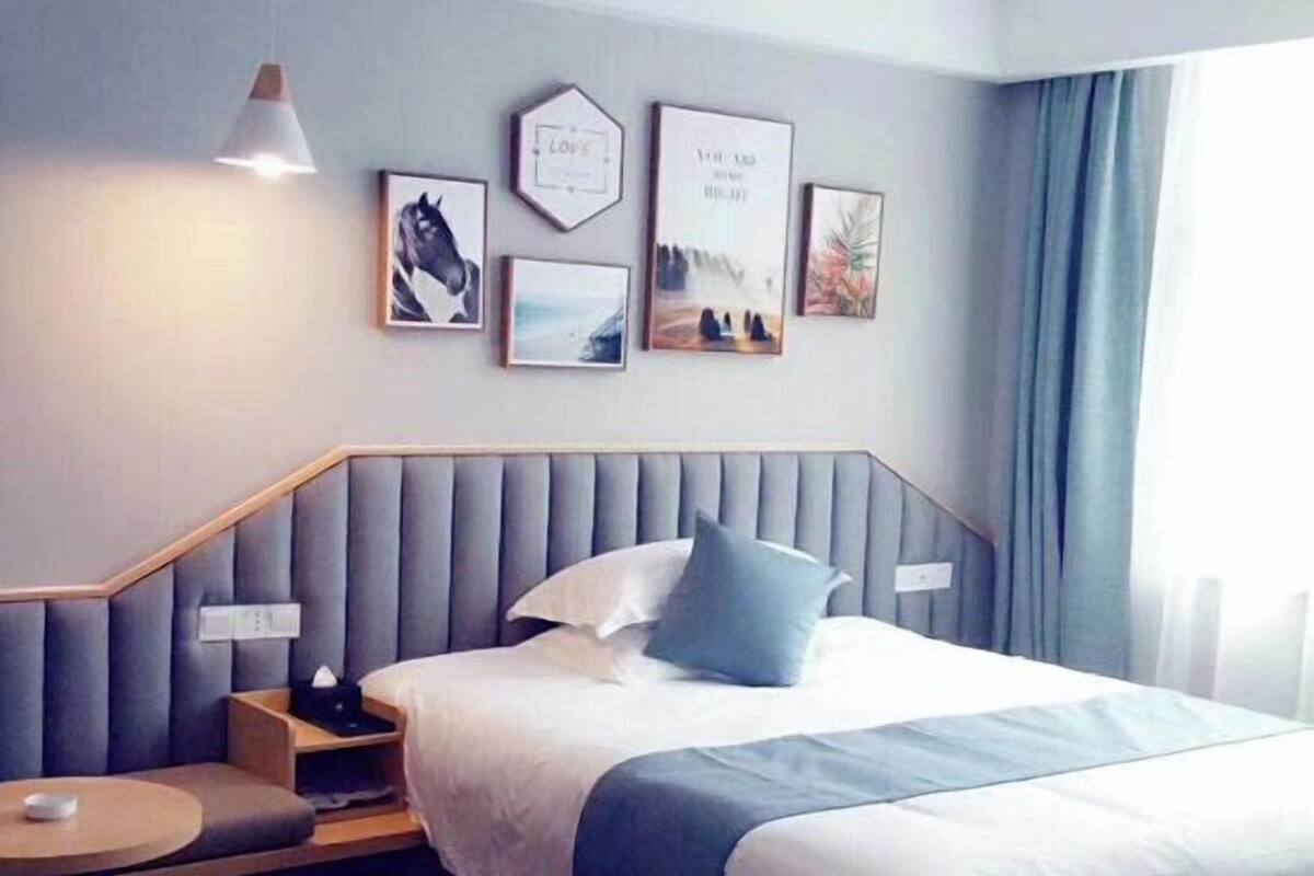 A modern hotel room with a large bed, bedside tables, a small seating area, and artwork on the walls.