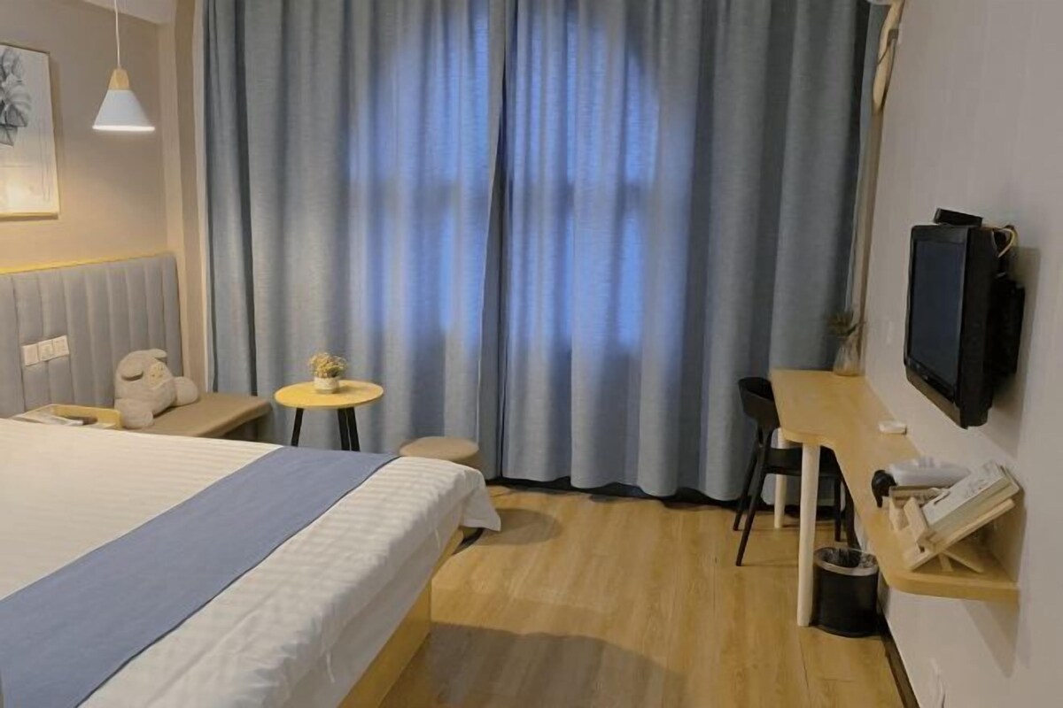 Une chambre d’hôtel avec un lit, une petite table, une chaise, un téléviseur et un rideau.