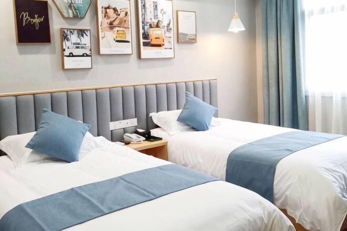 A hotel room with two beds, a grey headboard, and a nightstand with a phone and lamp.