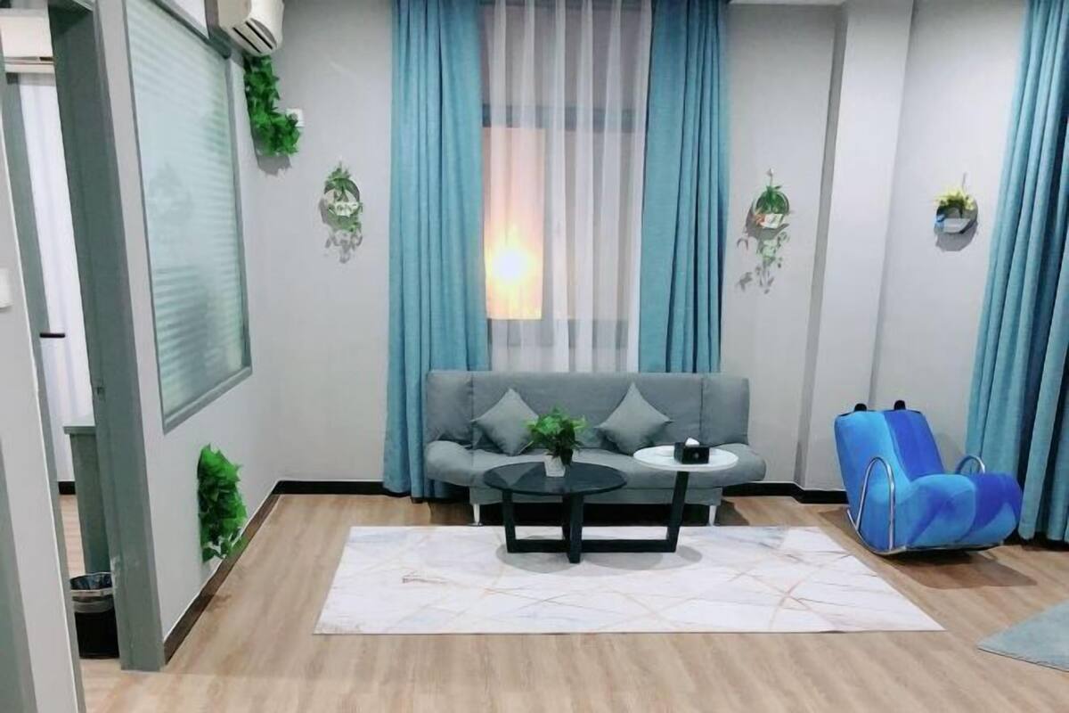 A modern living room with a grey sofa, a round coffee table, a blue chair, and a window with sheer curtains.