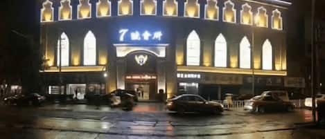 A building with a large arched entrance, illuminated signage, and a wet ground surface.