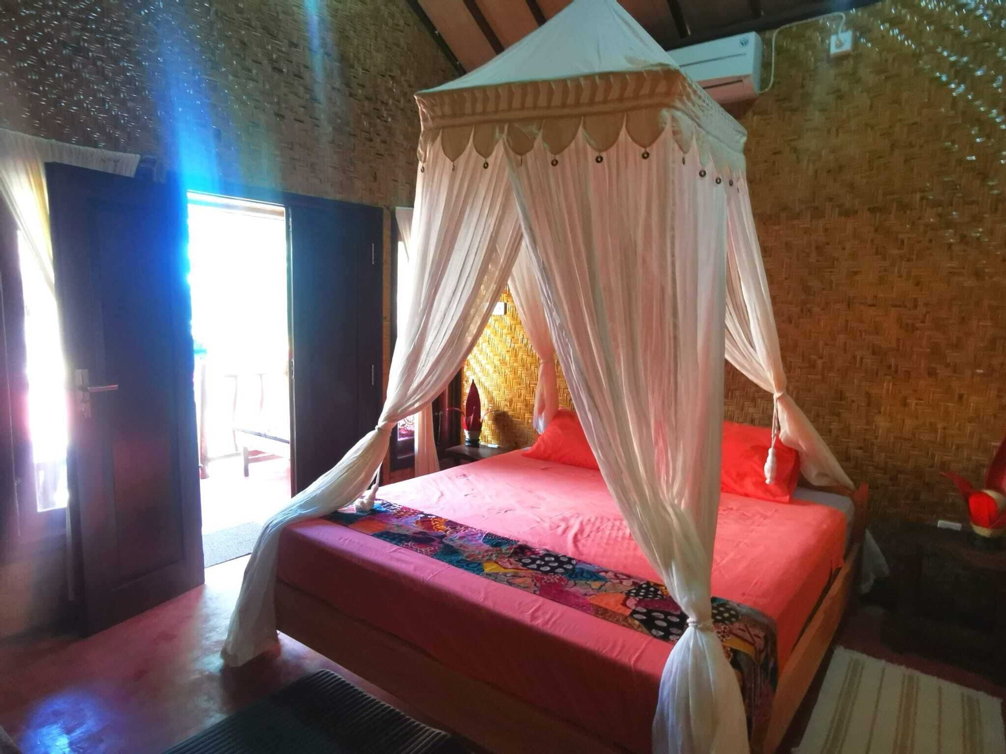 A bedroom with a bed covered by a canopy, a red bedspread, and a colorful quilt.