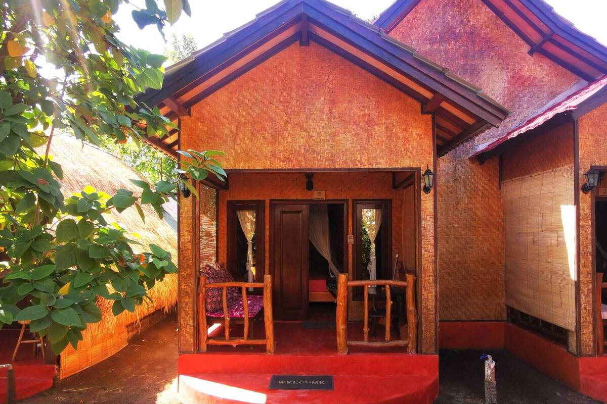 Un edificio tradicional con fachada roja, un porche de madera con dos sillas y un felpudo.