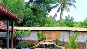 Zwembad met waterval, omgeven door een houten omheining en tropische beplanting.