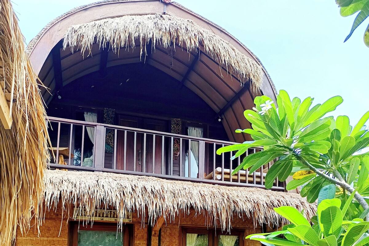 Una casa tradicional con techo de paja, un balcón y un jardín con plantas en macetas.