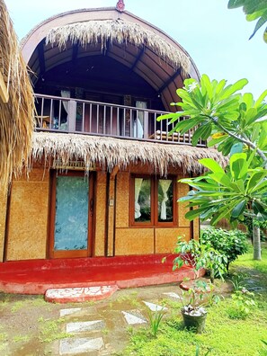 A traditional house with a thatched roof, a balcony, and a garden area with potted plants.
