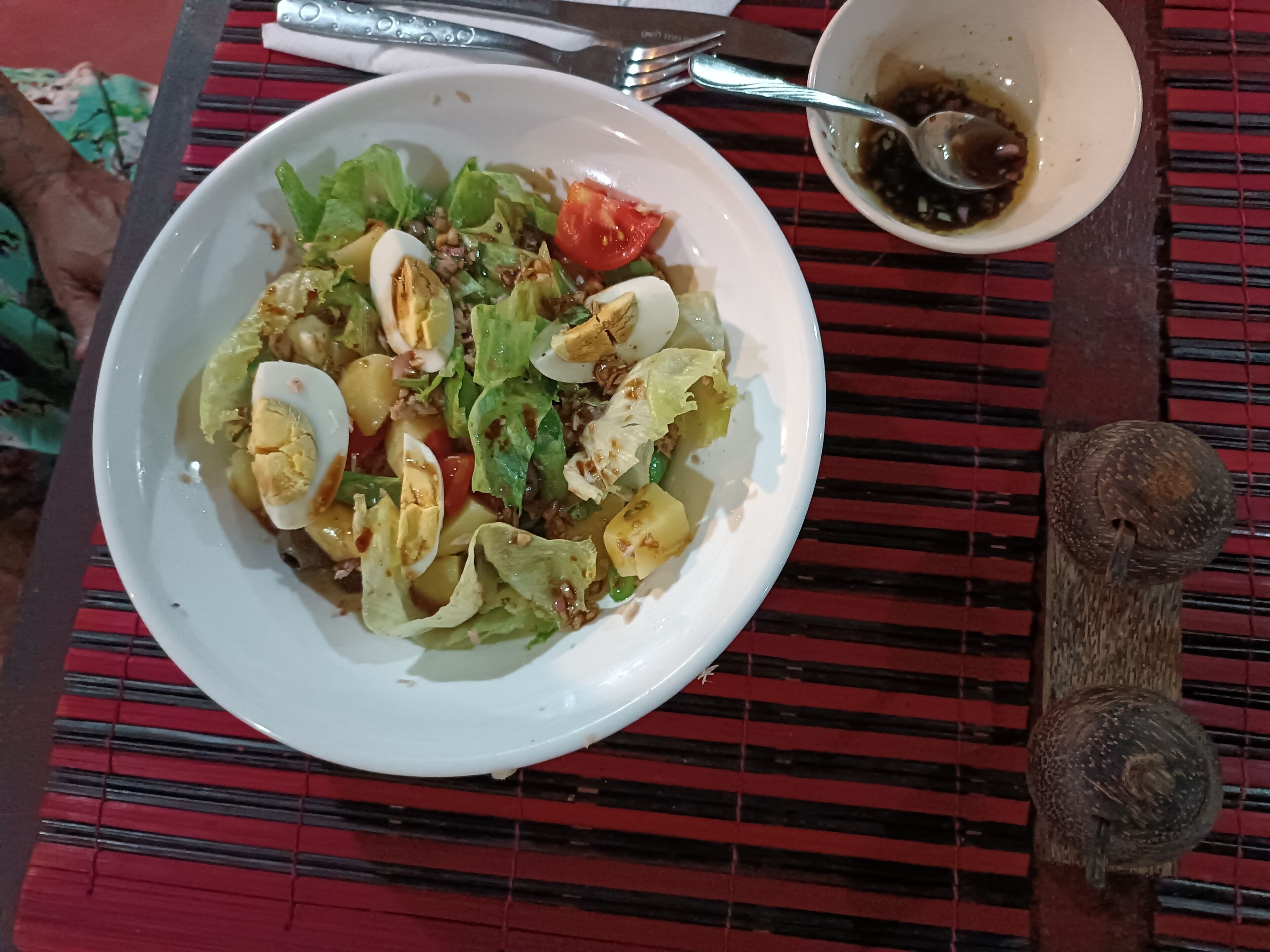 Un tazón blanco con ensalada de huevos, lechuga y tomates sobre un mantel a rayas rojo y negro.