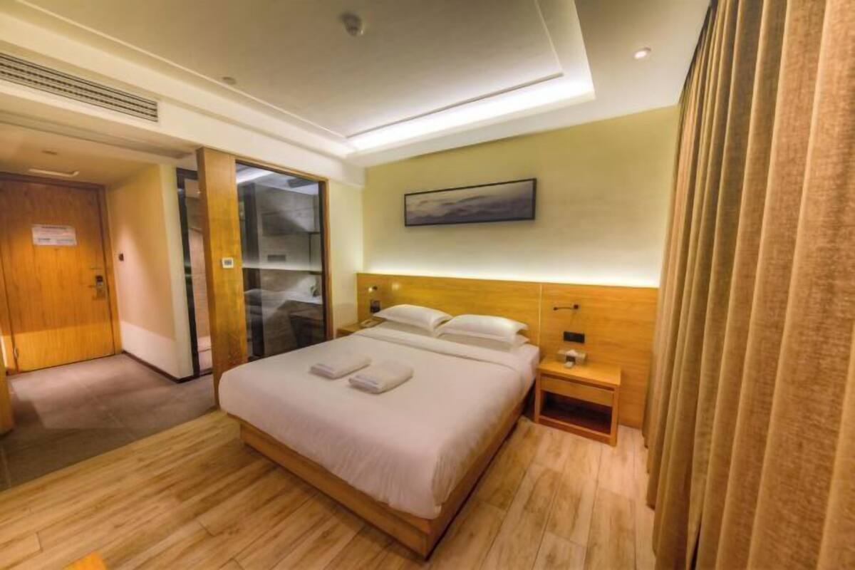 A hotel room with a bed, bedside tables, a wardrobe, and a painting on the wall.