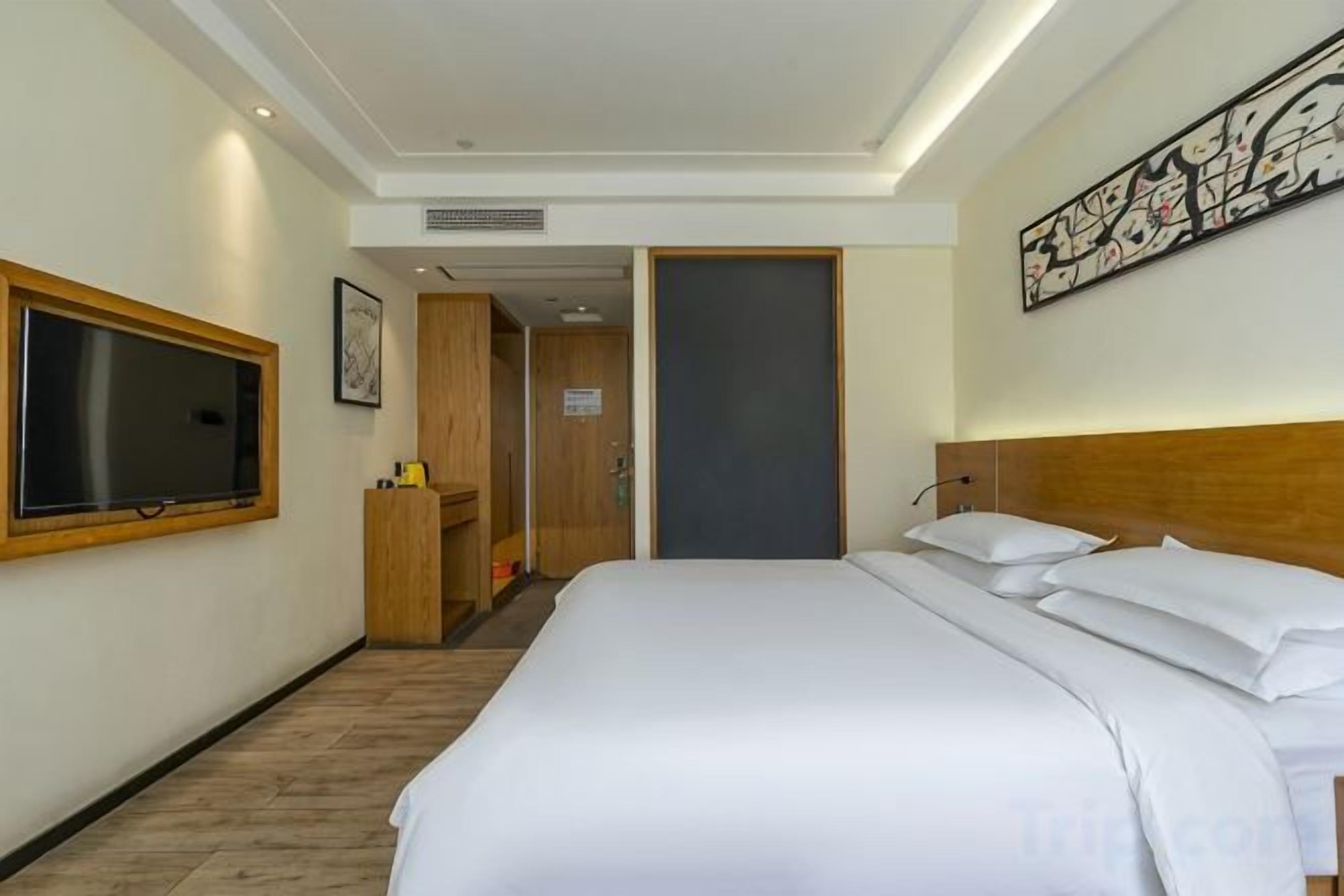A hotel room with a large bed, a television, a desk, and a door leading to a bathroom.