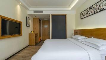 A hotel room with a large bed, a television, a desk, and a door leading to a bathroom.