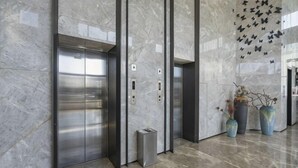 Un ascenseur moderne doté de portes métalliques, d’un mur en marbre et de vases décoratifs.