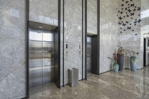 A modern elevator with metallic doors, a marble wall, and decorative vases. - Midor Hotel (Honggutan Wanda Plaza) (Nanchang)