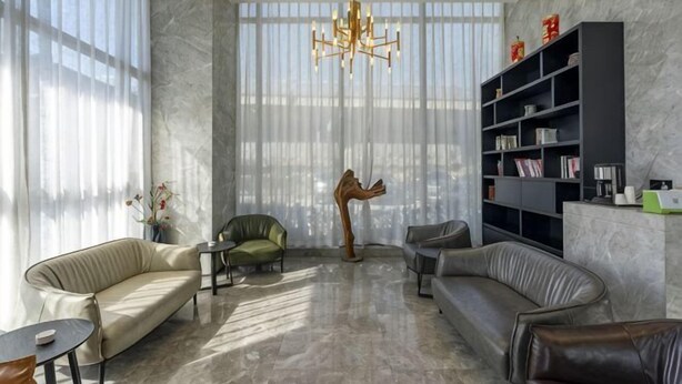 Un salon moderne comprenant un canapé, des fauteuils, une table basse, une bibliothèque et un lustre.
