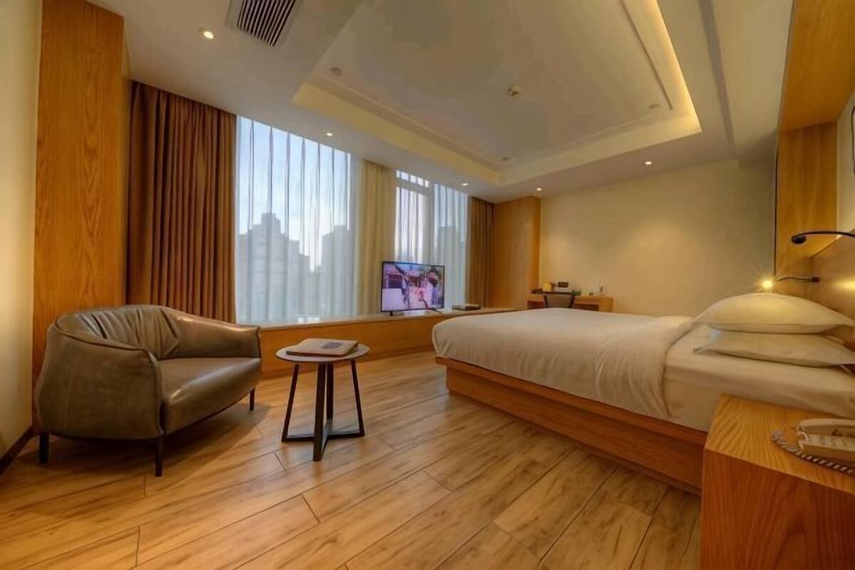 A hotel room with a bed, a sofa, a small table, a TV, and a city view.