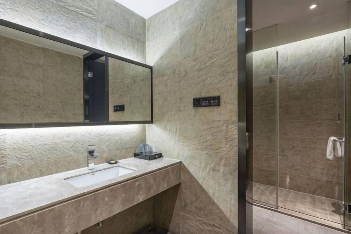 A modern bathroom with a large mirror, a sink, and a glass shower enclosure.