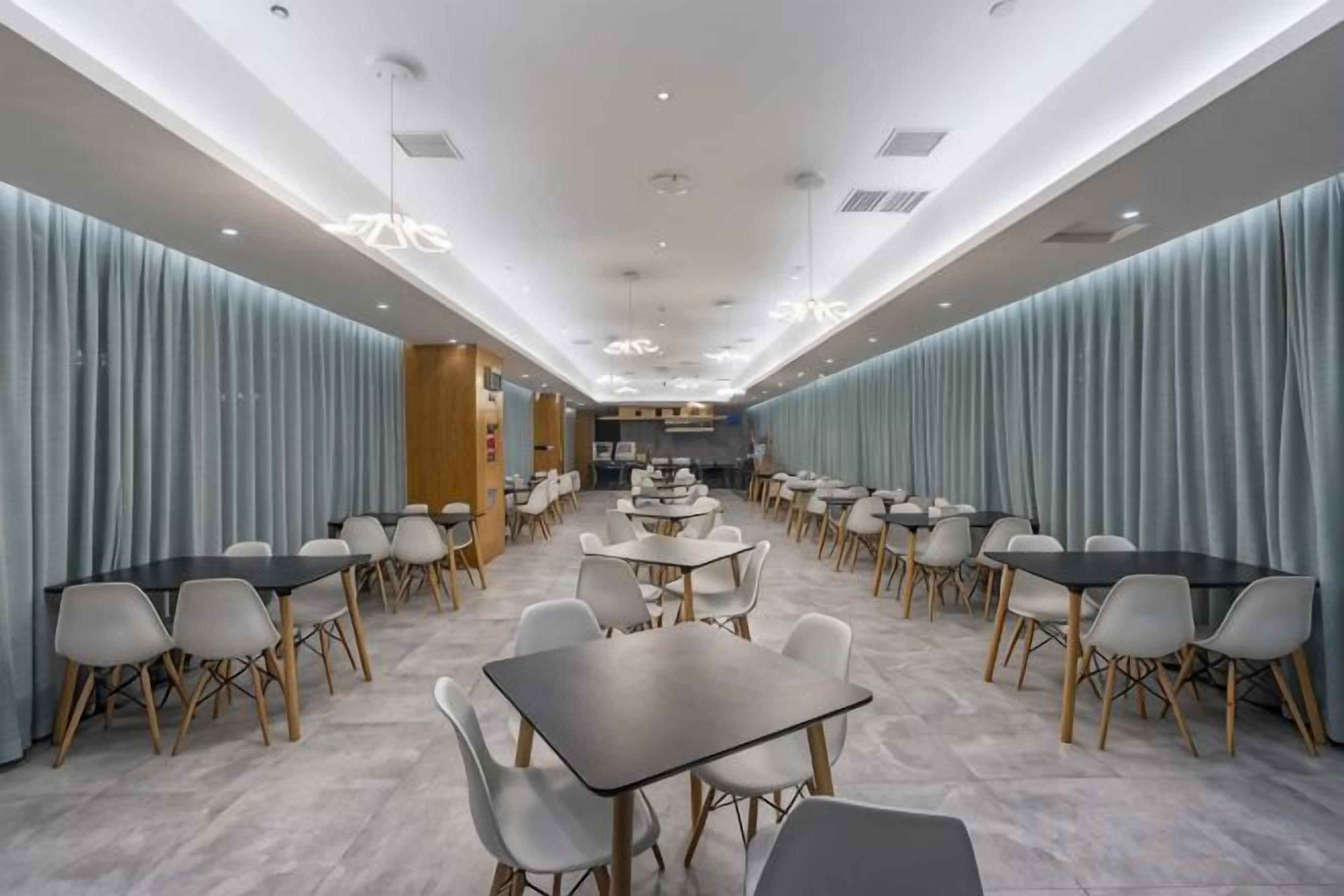 A spacious dining area with multiple tables and chairs, a central kitchen area, and a modern ceiling design.